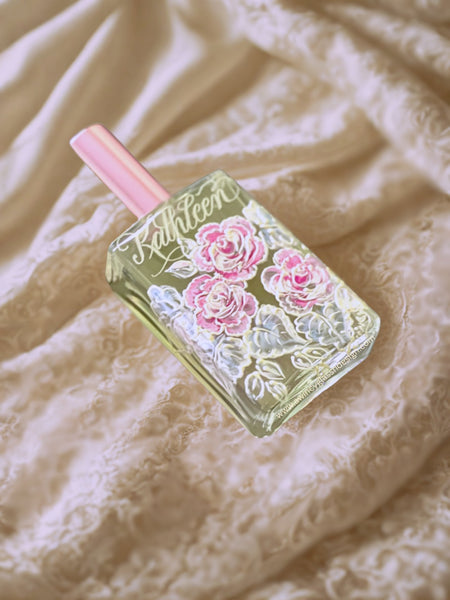 Engraved and hand-painted refillable perfume bottle featuring delicate pink roses, displayed on layered lacy fabric folds — a luxury personalized gift for brides, bridesmaids, mothers of the bride, and bridal parties, crafted by A Wincy Glass ’N Design
