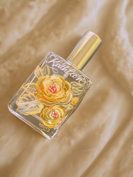 Flat lay of an engraved and hand-painted refillable perfume bottle featuring elegant peach ranunculus florals on a warm champagne ivory background — a luxury personalized gift for brides, bridesmaids, and mothers of the bride, crafted by A Wincy Glass ’N Design.”