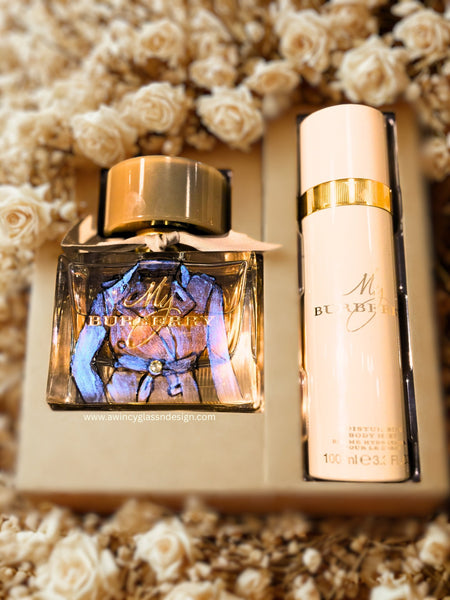 Custom hand-painted Burberry perfume gift set featuring the iconic Burberry trench jacket design in soft beige and black detailing, accented with a Swarovski crystal at the tied waist. Displayed inside its original Burberry gift box with the lid removed, the perfume and lotion set embodies timeless British elegance — a couture-inspired personalized perfume art piece for brides, collectors, and luxury gift-givers, handcrafted by A Wincy Glass ’N Design.