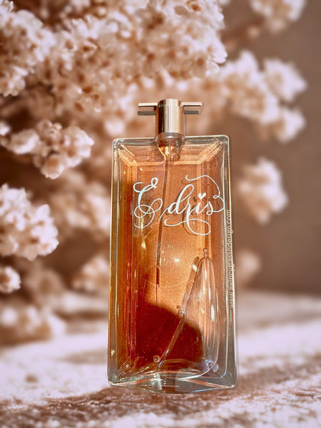 Personalized Lancôme Idôle fragrance bottle with custom engraving, staged on a tabletop with delicate white florals; airy, romantic lighting evokes a wedding-ready scene—perfect for bridal gifts, keepsakes, and bridesmaid proposals.