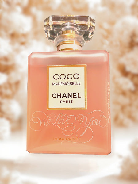 Personalized engraved Chanel-style perfume bottle,” against a soft backdrop of, blurred pale roses in an elegant bridal editorial aesthetic; ideal gift for brides, bridesmaids, and proposal boxes.